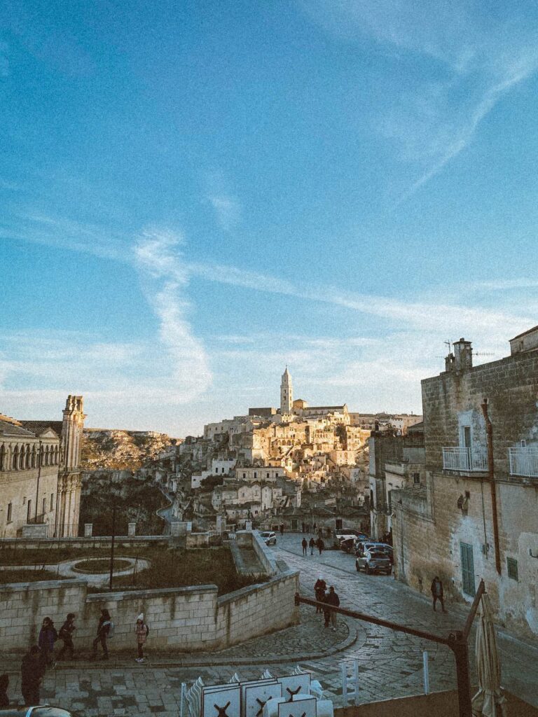 Matera in una giornata soleggiata, scorcio del centro storico con cielo sereno e alcune persone che passeggiano